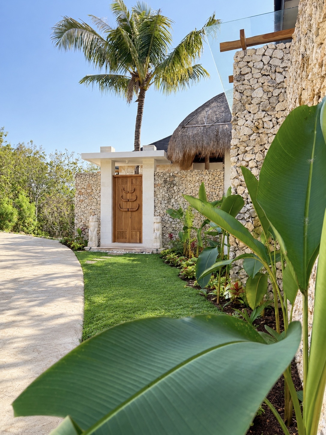 Villa exterior with stone wall, teak door and thatch roof