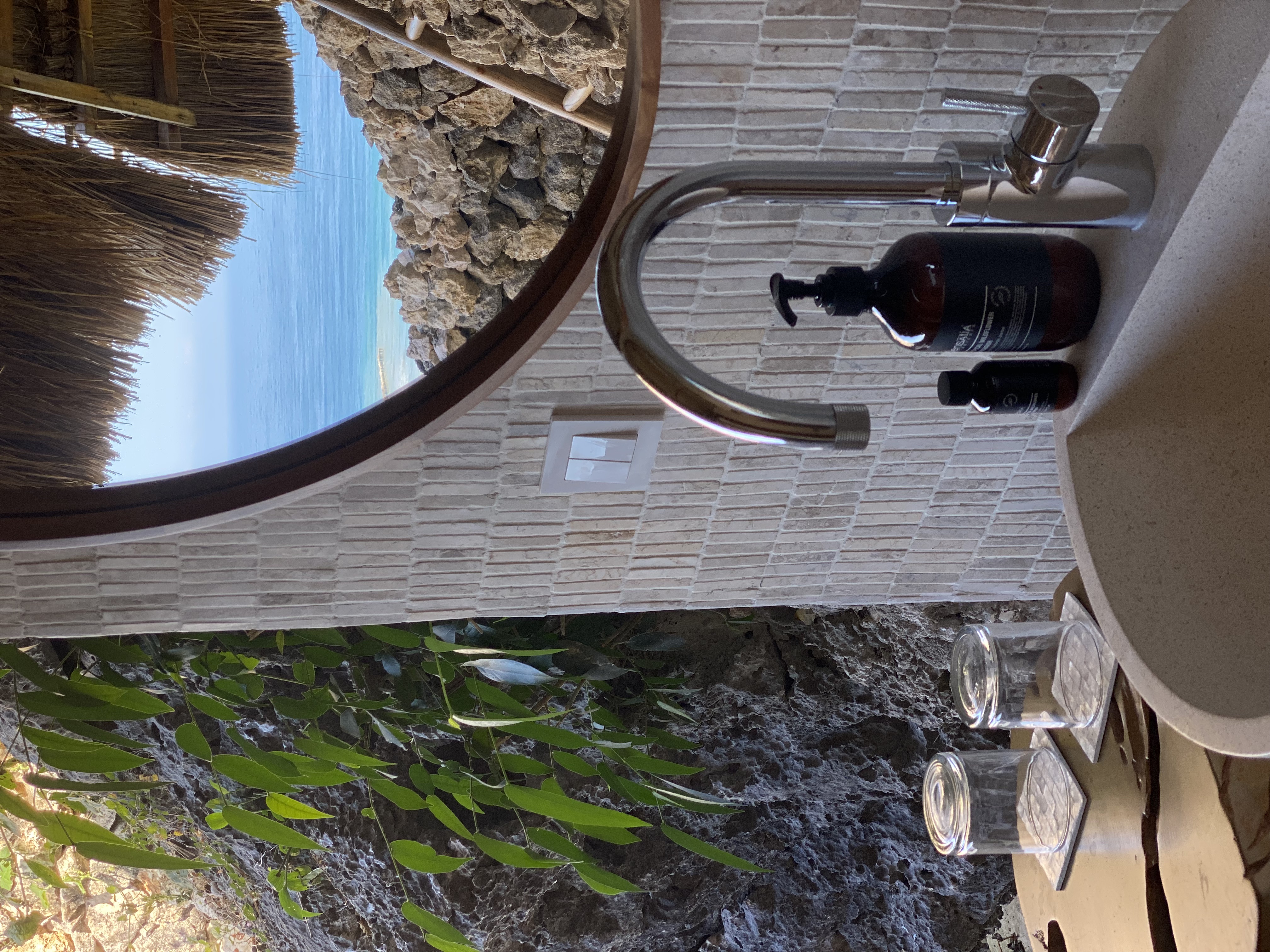 Bathroom sink detail with round mirror reflecting the sea