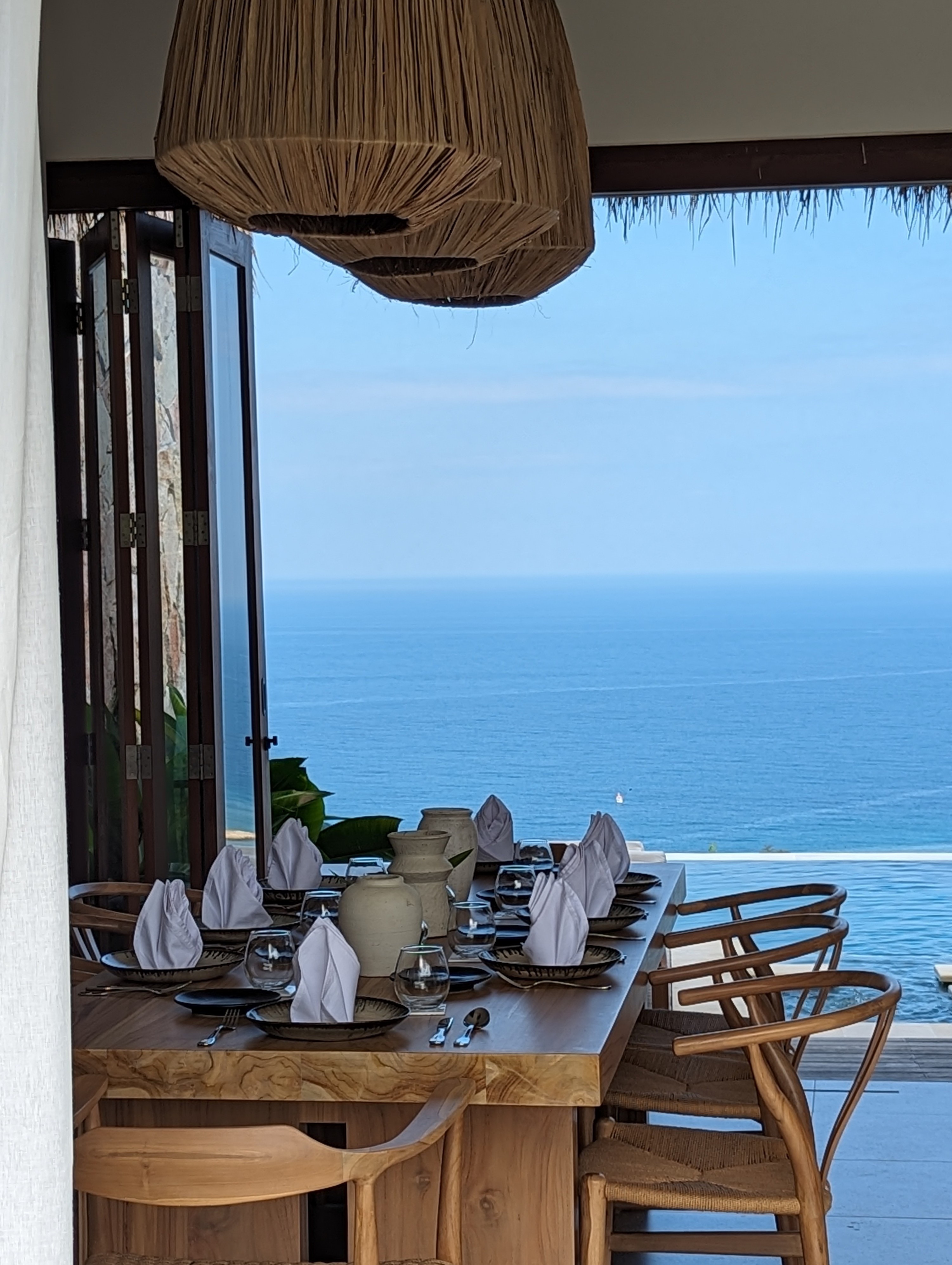 Dining table with thatched pendant lamp facing the sea